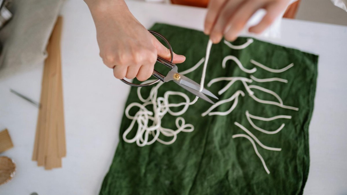 Close-up of hands cutting candle wicks on green fabric, showcasing craft skills.