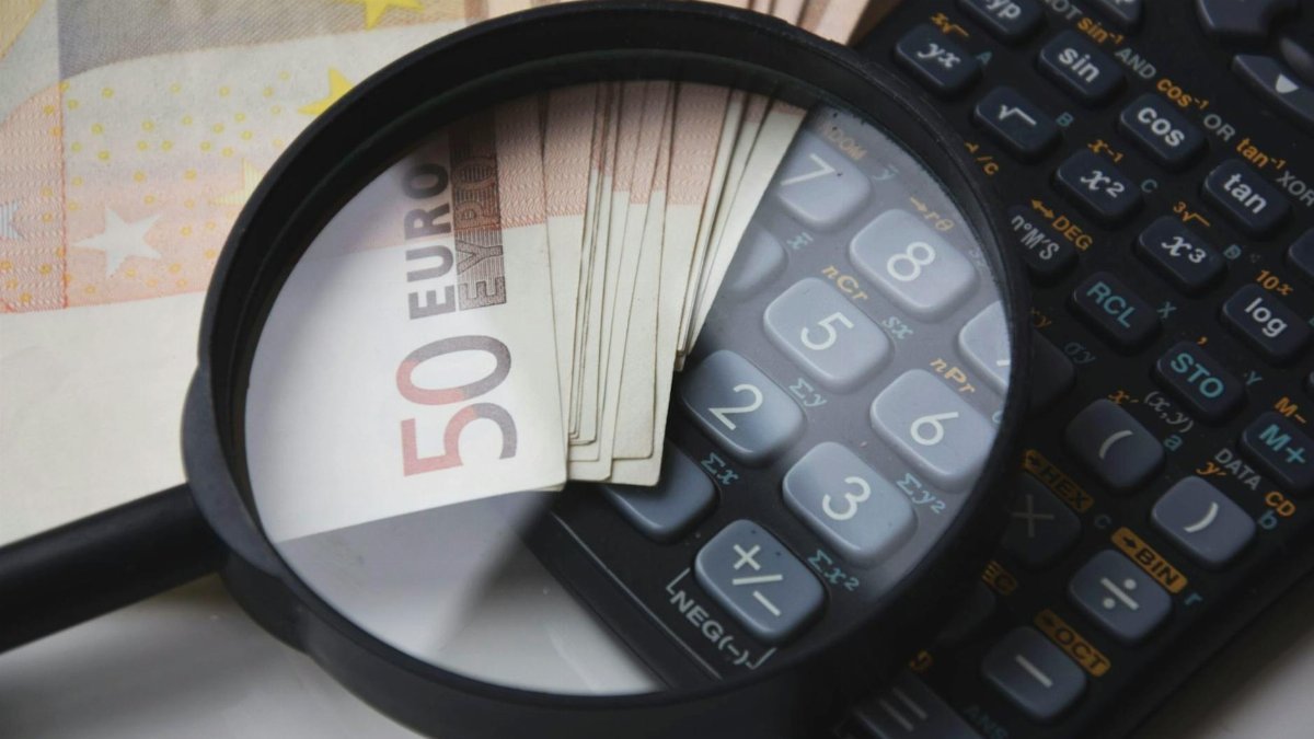 Euro bills under magnifying glass with calculator, symbolizing finance and analysis.