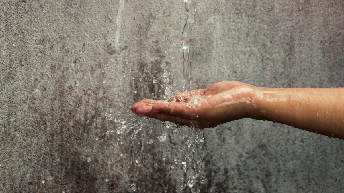 Hand catching a stream of water against a textured wall background.