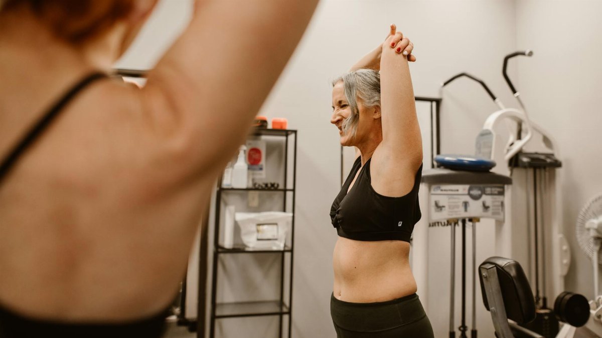 A middle-aged woman confidently stretches in a gym, embracing wellness and healthy living.