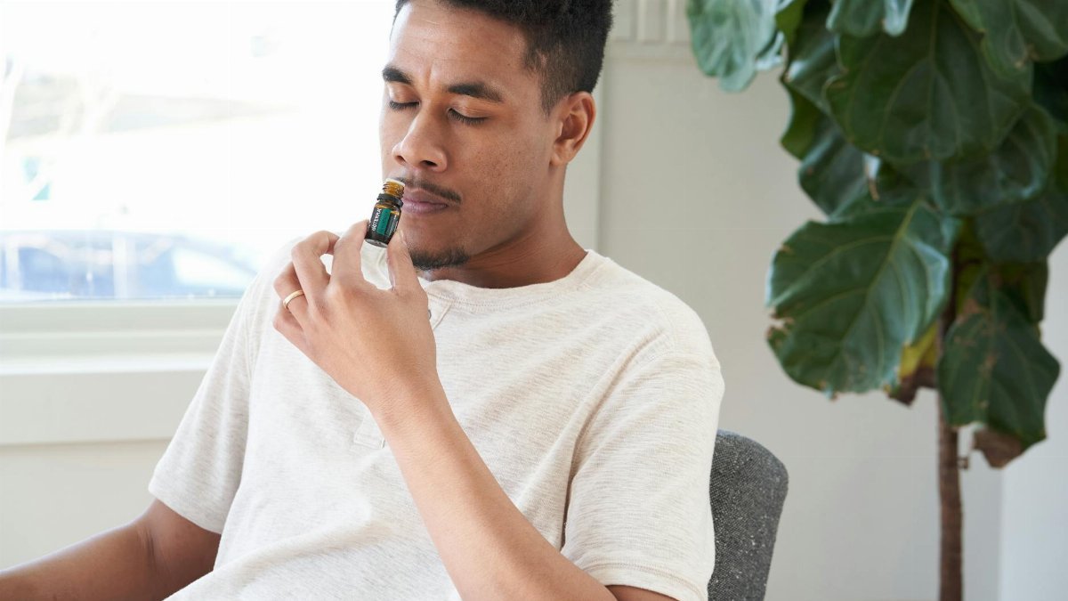 A man in a white shirt enjoys the scent of essential oil beside a green plant.