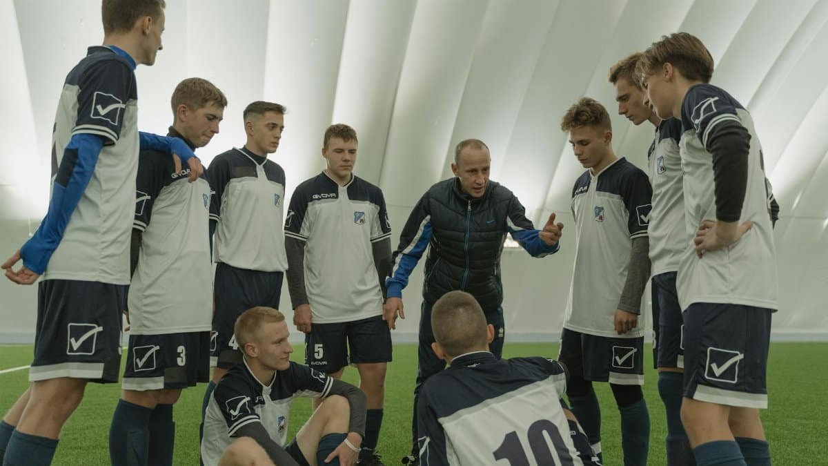 Coach giving a pep talk to a men's soccer team indoors.