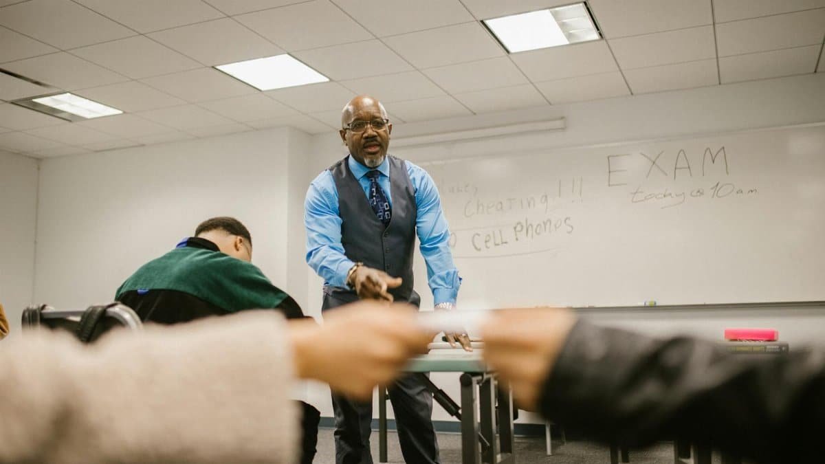 Students interacting with a teacher in a classroom during an exam, focusing on academic integrity.