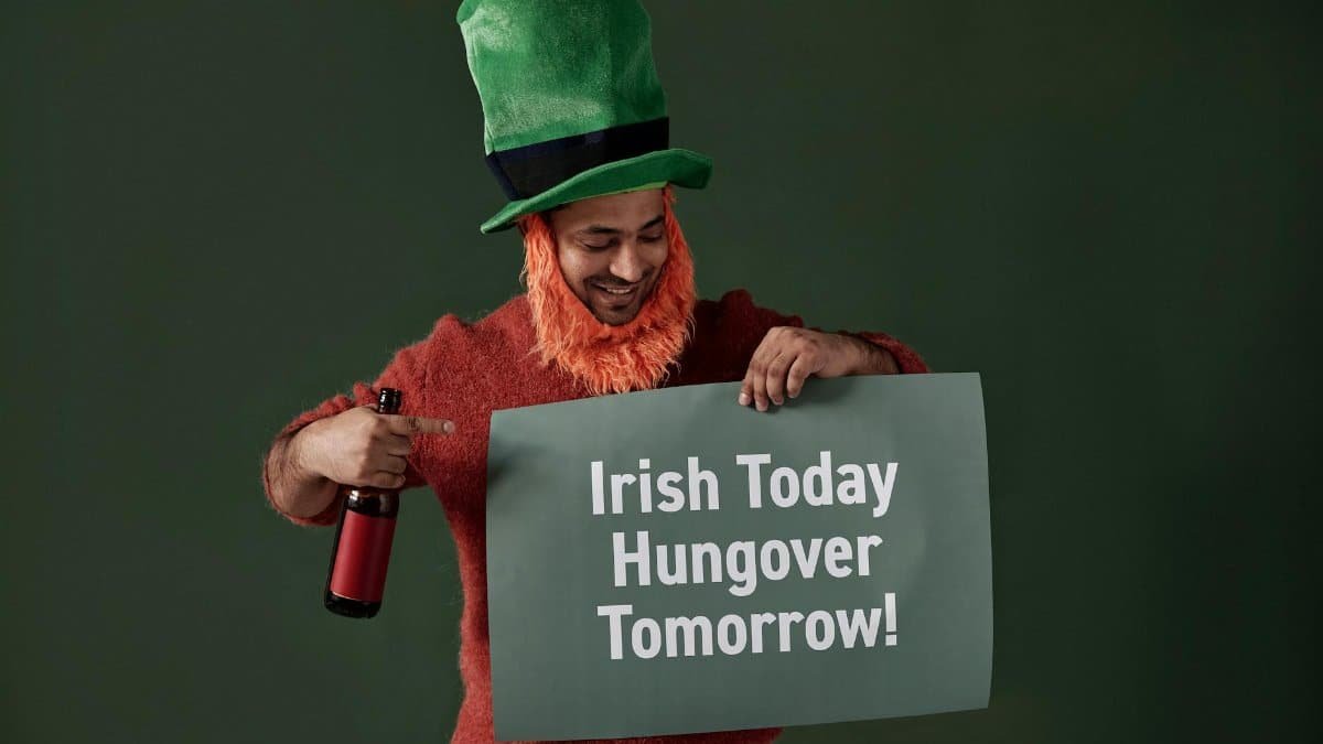Happy man dressed as a leprechaun holding a themed sign and drink.