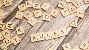 Wooden letter tiles arranged to spell 'Rules' on a textured wooden background.