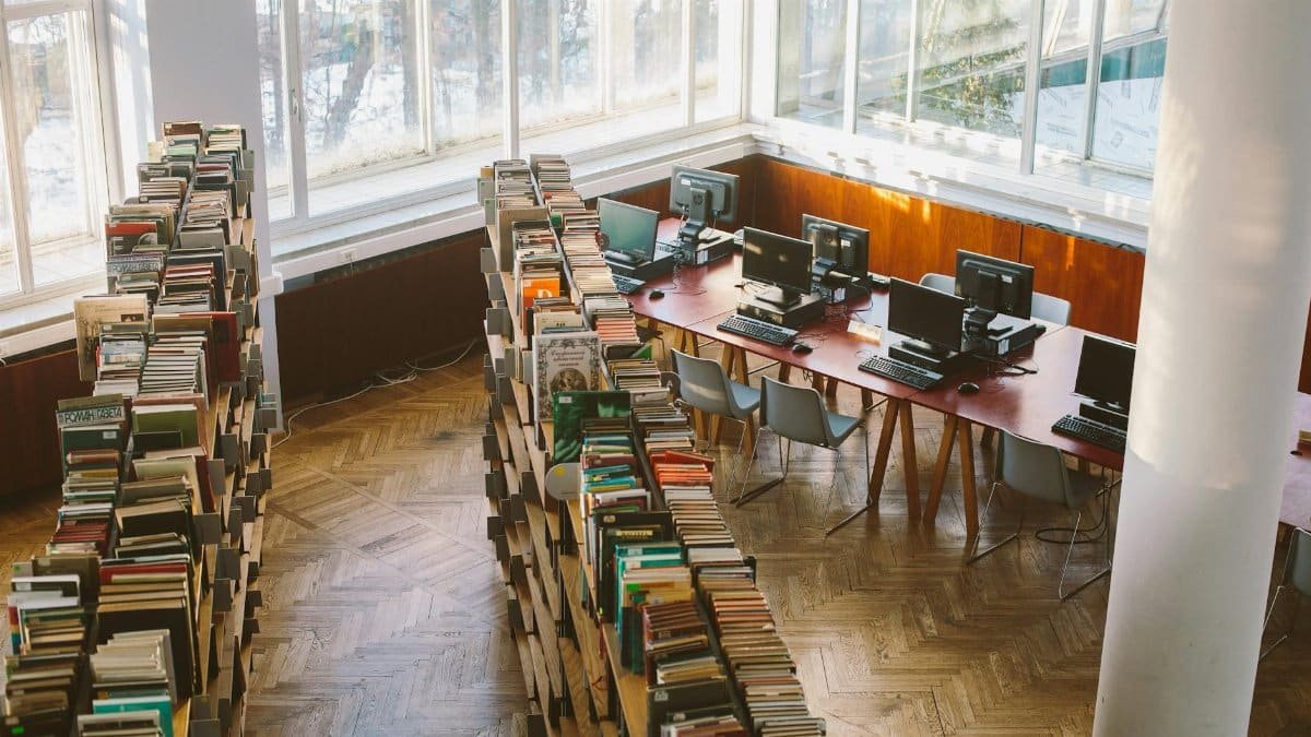 A university library viewed from above, featuring bookshelves and computer stations under natural daylight.