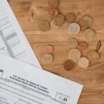 Flat lay of tax forms and scattered coins on a wooden table, illustrating finance and taxation concepts.