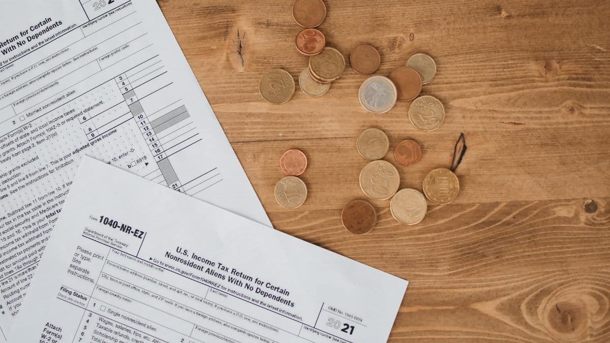 Flat lay of tax forms and scattered coins on a wooden table, illustrating finance and taxation concepts.