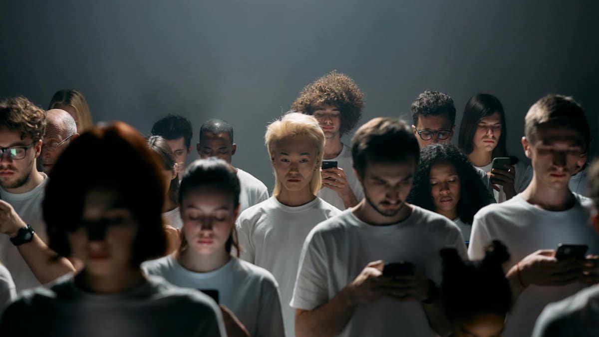 A diverse crowd focused on smartphones, illustrating social isolation and technology connection.