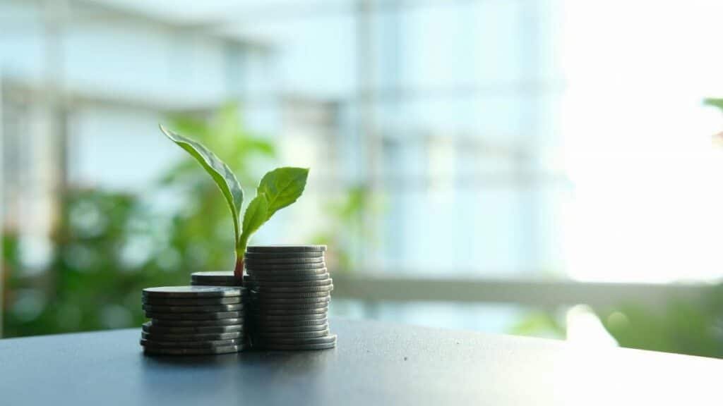A small plant sprouting from stacked silver coins, symbolizing growth in finance.