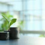 A small plant sprouting from stacked silver coins, symbolizing growth in finance.