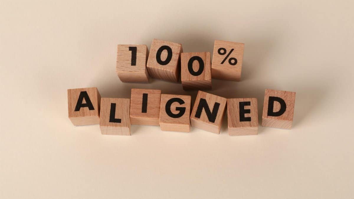 Wooden blocks spelling '100% Aligned' on a neutral background, conveying precision and alignment.