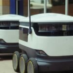 Two autonomous delivery robots positioned outside a modern building, showcasing innovation in robotics and mobility.