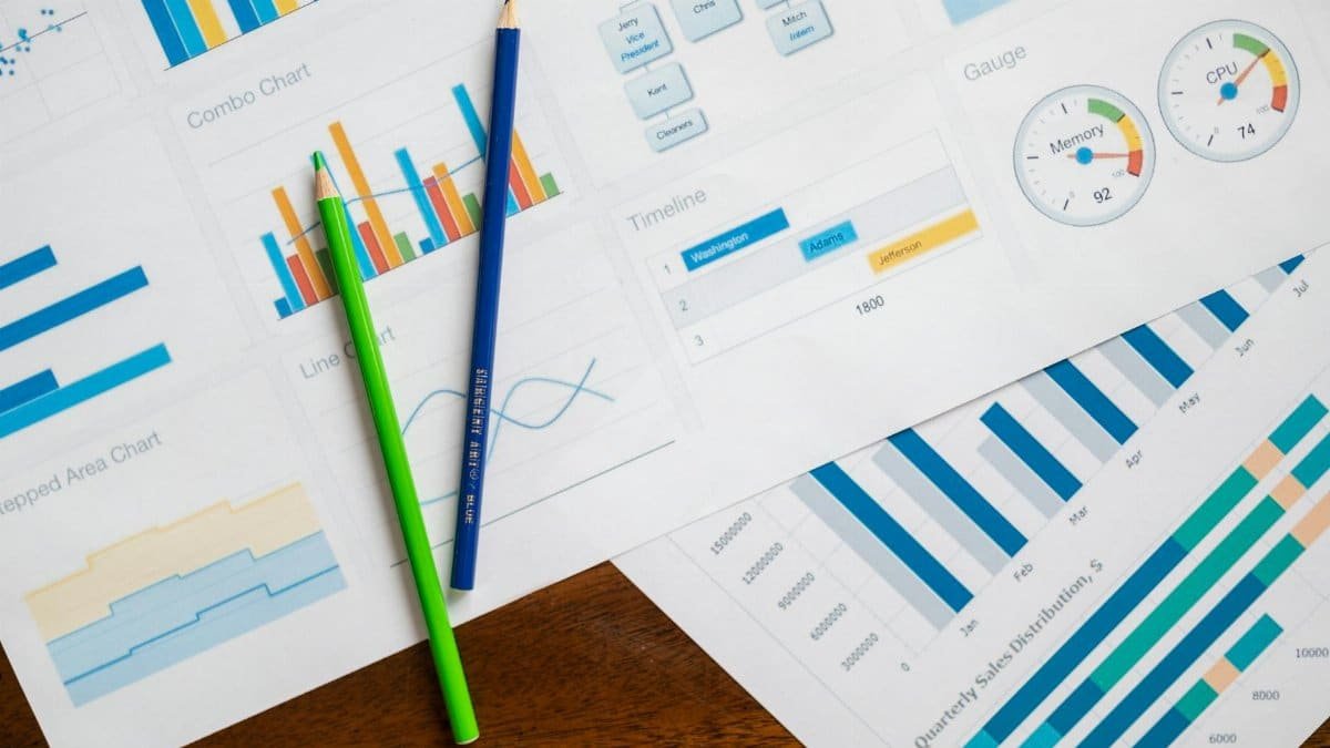 Flat lay of various business charts and colored pencils on wooden table, highlighting financial analysis.