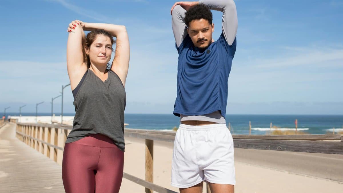 Two adults stretching on a sunny beach boardwalk, capturing an active lifestyle.