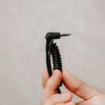 Closeup of a hand holding a coiled audio cable plug against a neutral background.