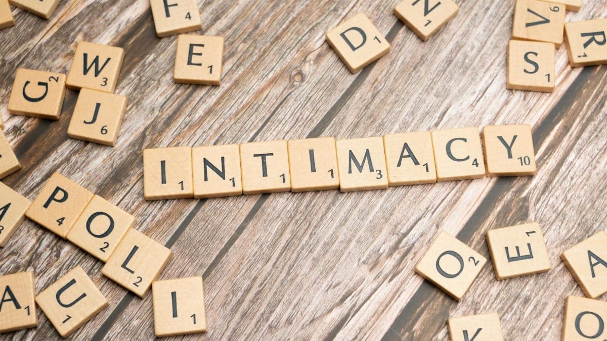 Scrabble tiles arranged to form the word 'intimacy' on a wooden background.