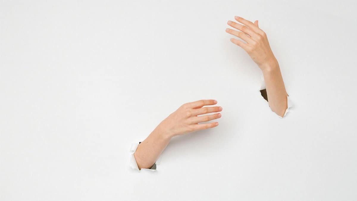 Two hands emerging through a white surface, symbolizing creativity and breakthrough concepts.