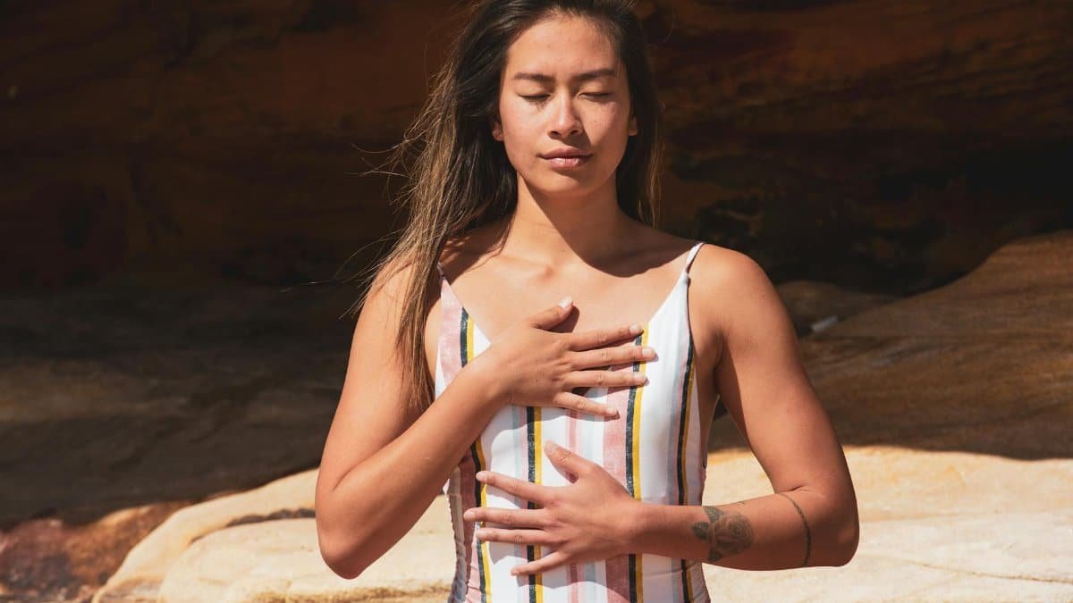 A woman relaxes with chest breathing outdoors, eyes closed in meditative state.