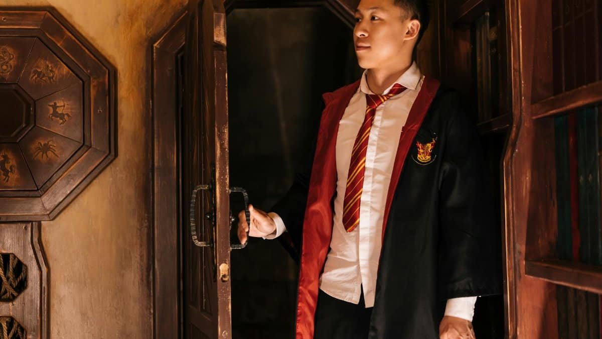 A young man in wizard attire opens a wooden door, creating an air of mystery.