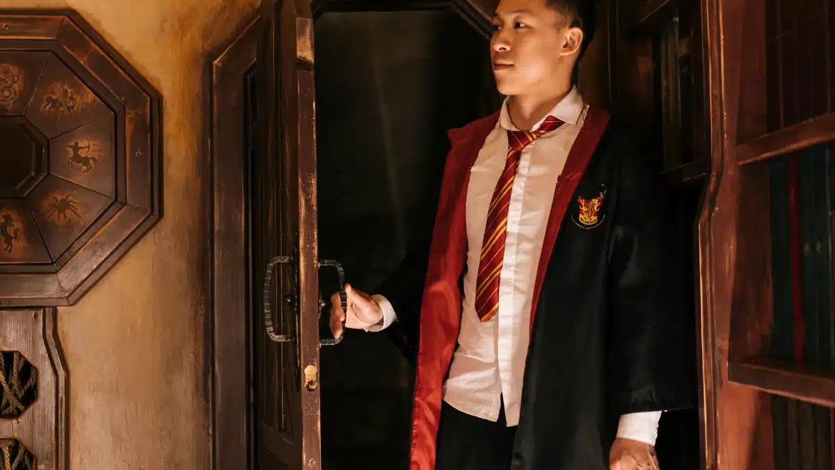 A young man in wizard attire opens a wooden door, creating an air of mystery.