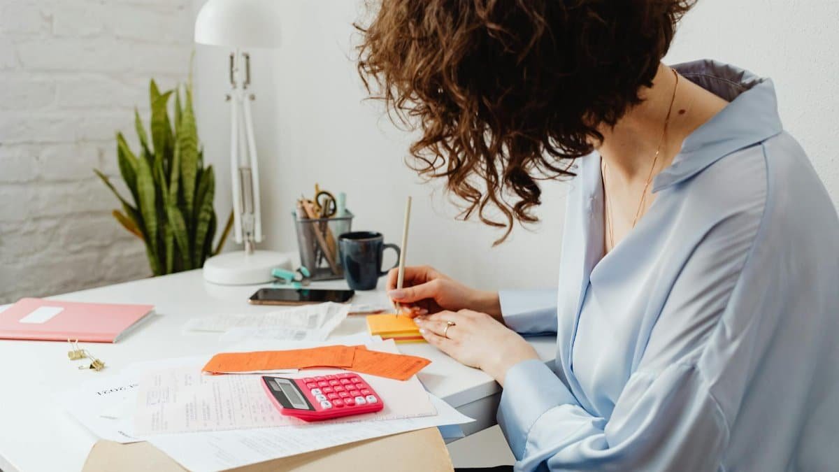 Woman writing with calculator on desk, managing finances indoors.