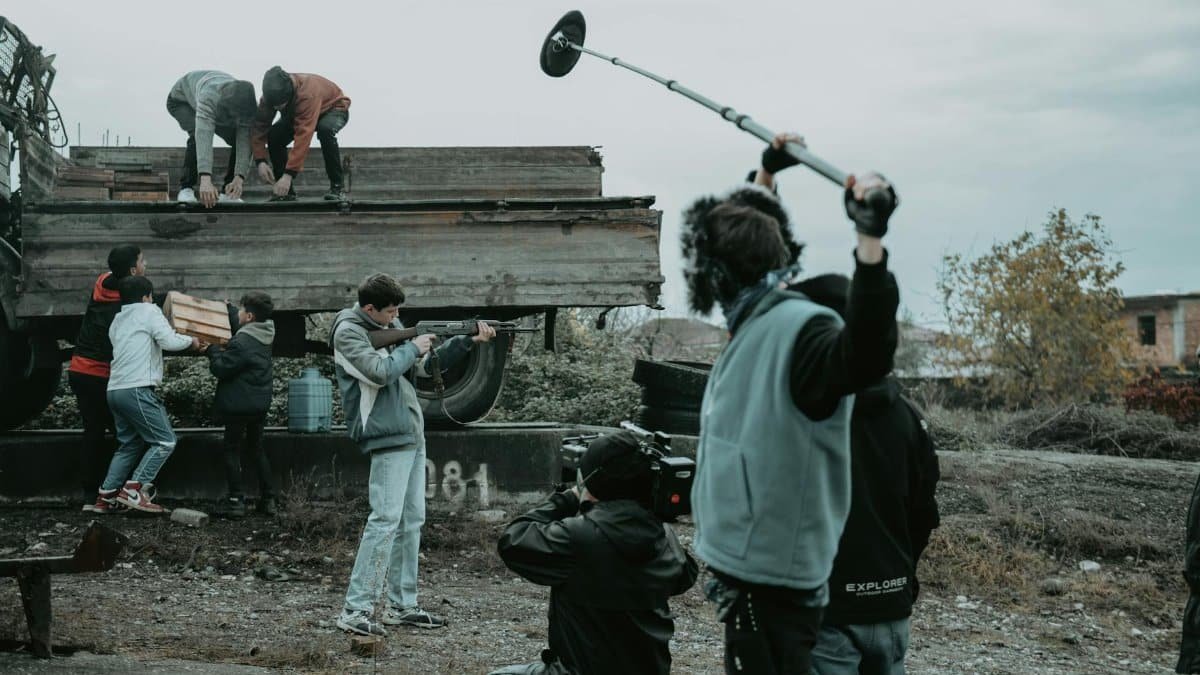 Film crew working outdoors, capturing scenes with camera and boom mic.