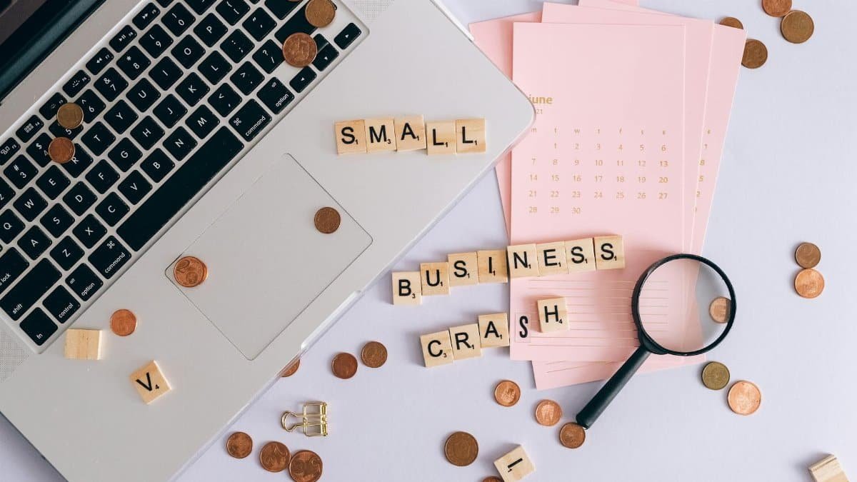Flatlay of a laptop, coins, and scrabble tiles spelling 'small business crash'.