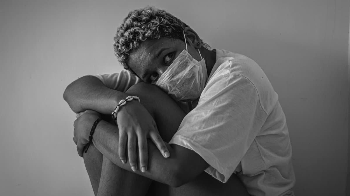 A person seated, wearing a face mask, expressing anxiety in a grayscale photograph.