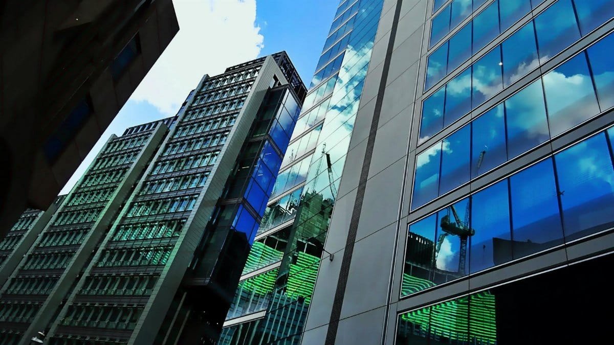 Low angle view of modern skyscrapers with glass facades reflecting blue sky and clouds.