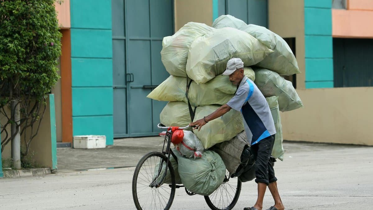 A man navigates a bicycle overloaded with large bags in a bustling city setting, illustrating urban life.