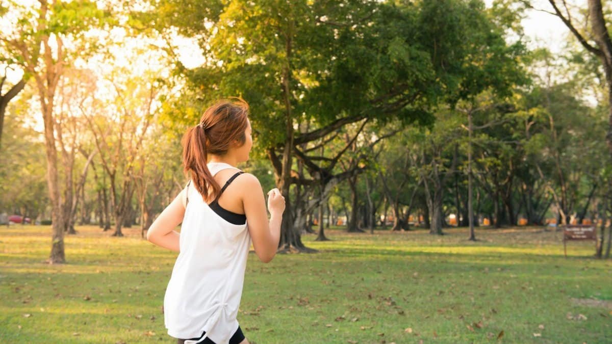 A woman jogging through a forest park in the early morning sunshine, enjoying a healthy lifestyle.
