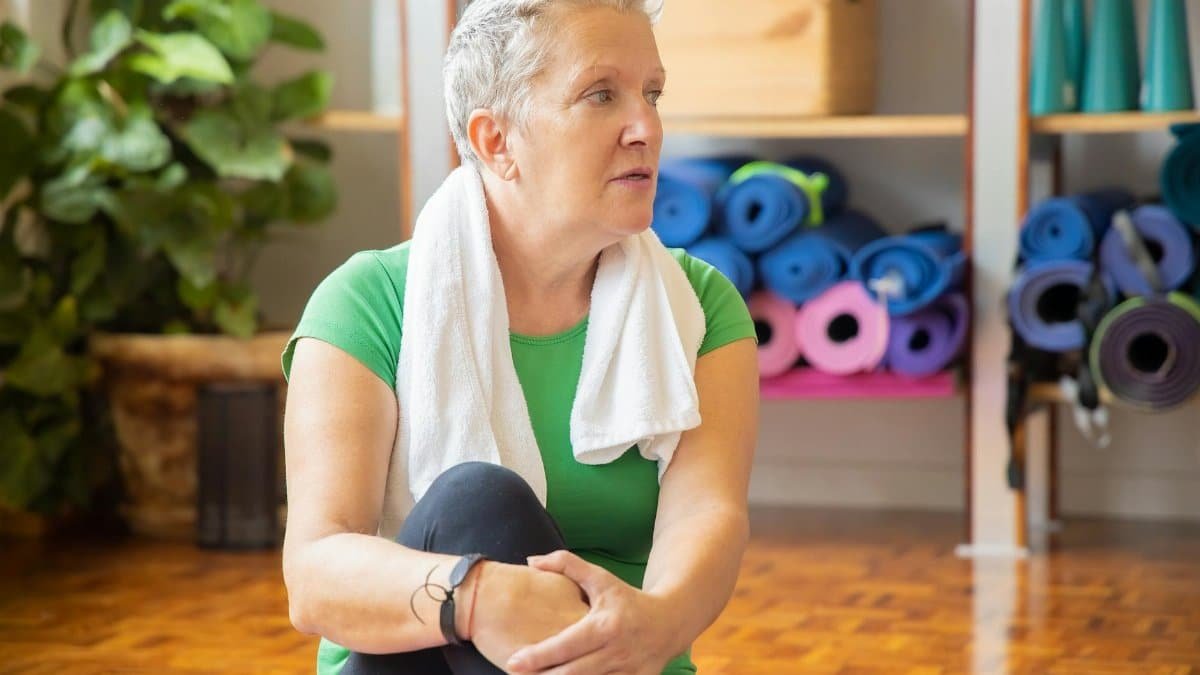 Senior woman relaxing after yoga session with yoga mats in the background. Indoor, health-focused setting.