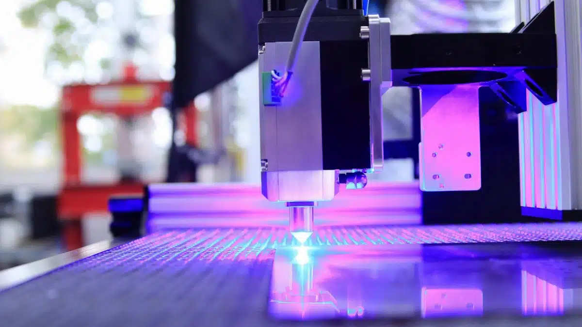Close-up of a laser engraving machine working indoors with blue light reflection.