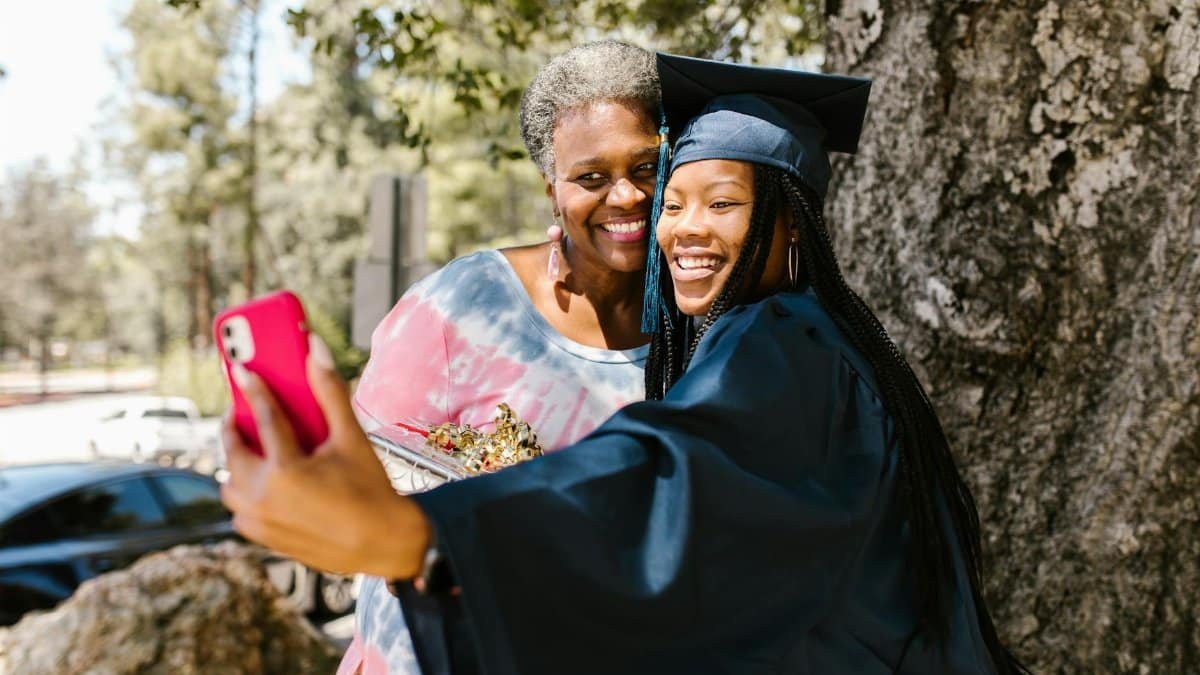A proud graduate takes a cheerful selfie with family outdoors, capturing a joyful graduation moment.