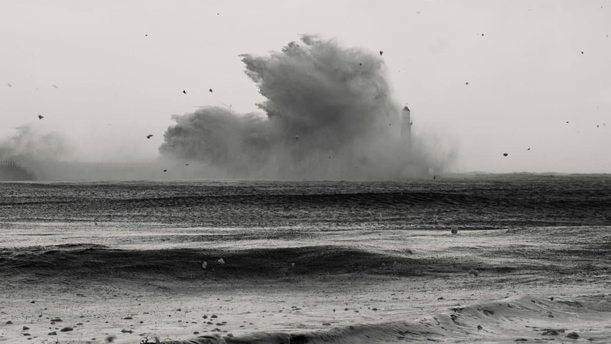 Captivating black and white image of a lighthouse standing strong against huge ocean waves during a storm.