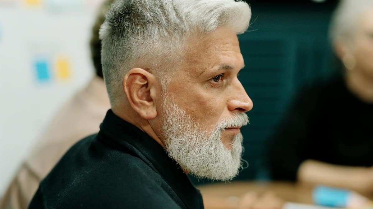 Profile view of an elderly man with gray hair at a meeting, focused and thoughtful.