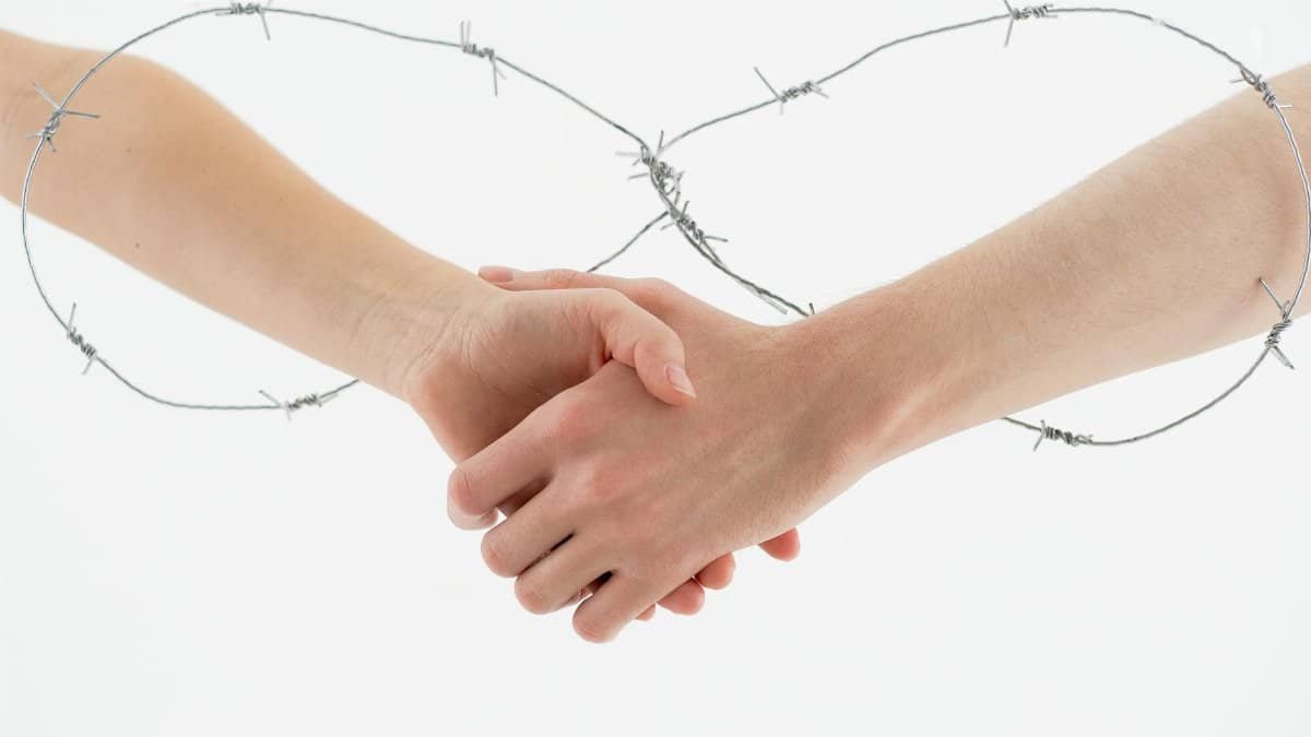 Symbolic handshake wrapped in barbed wire on a white background representing restriction and unity.