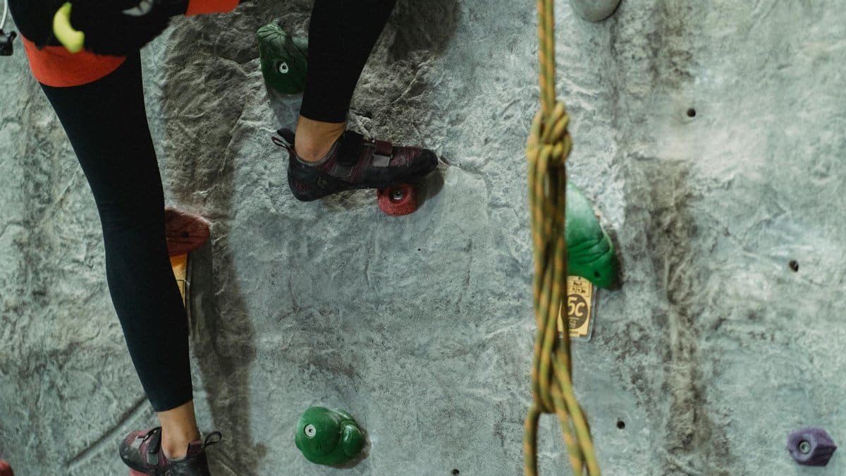 Crop anonymous risky female with belaying equipment training on stony gray climbing wall