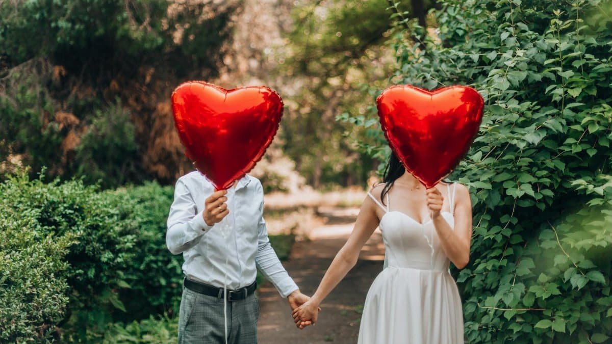 A couple holding red heart-shaped balloons outdoors, symbolizing love and romance.