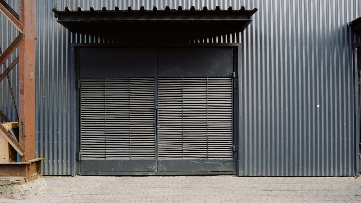 A corrugated metal door on an industrial warehouse exterior with a paver walkway.