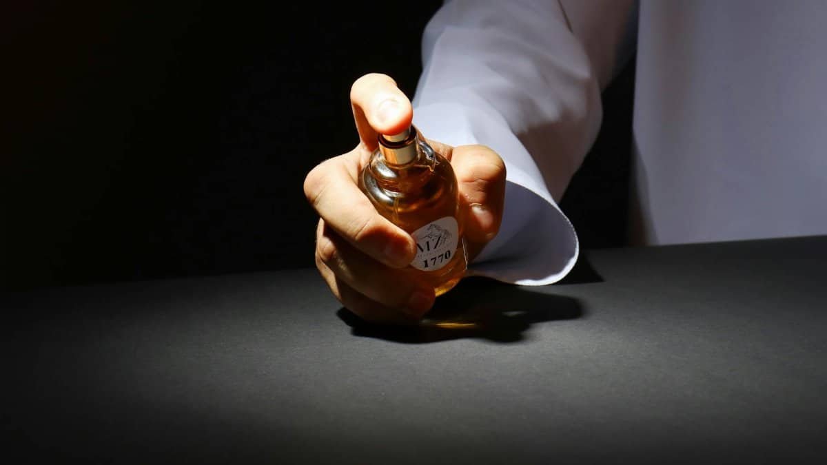A hand elegantly holding a perfume bottle against a dark backdrop, highlighting luxury fragrance.