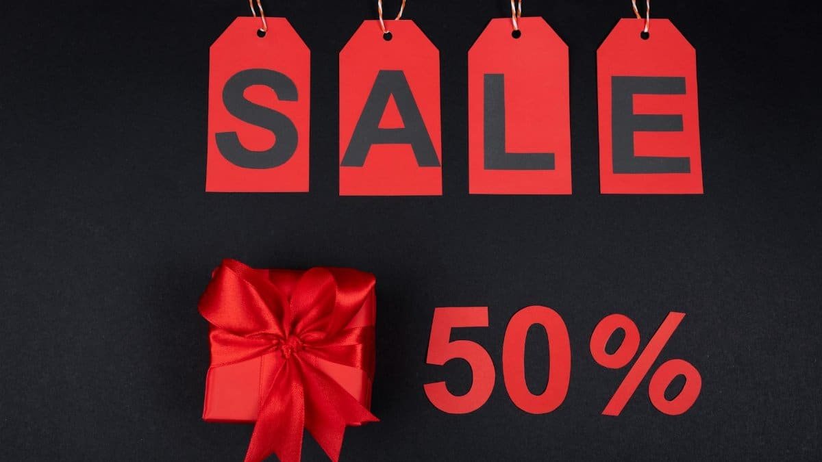 Red gift box next to sale tags and 50% sign on black background, ideal for promotions.