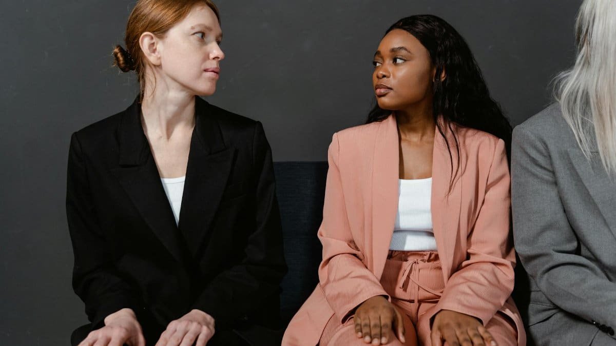 Three women in business suits sitting indoors against a gray background.