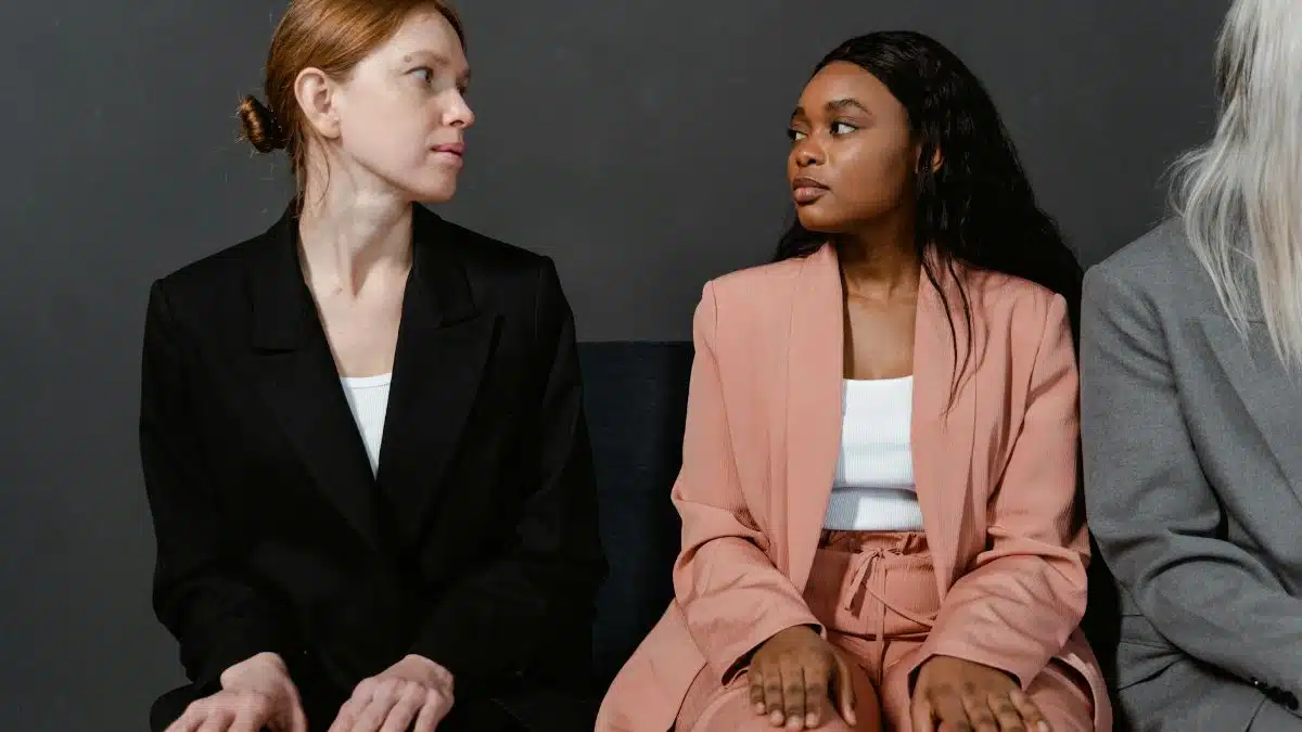 Three women in business suits sitting indoors against a gray background.