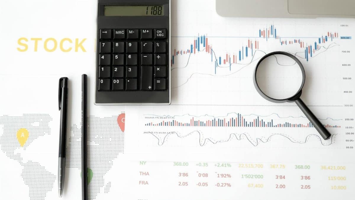 Flat lay of stock market analysis tools including calculator, graphs, and magnifying glass.