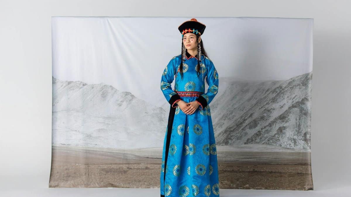 Young woman in traditional Mongolian attire with mountain backdrop, shot in studio.