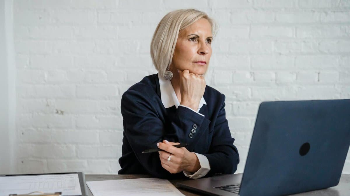 Professional woman in deep thought, working on a laptop indoors, suggesting mental focus and business acumen.