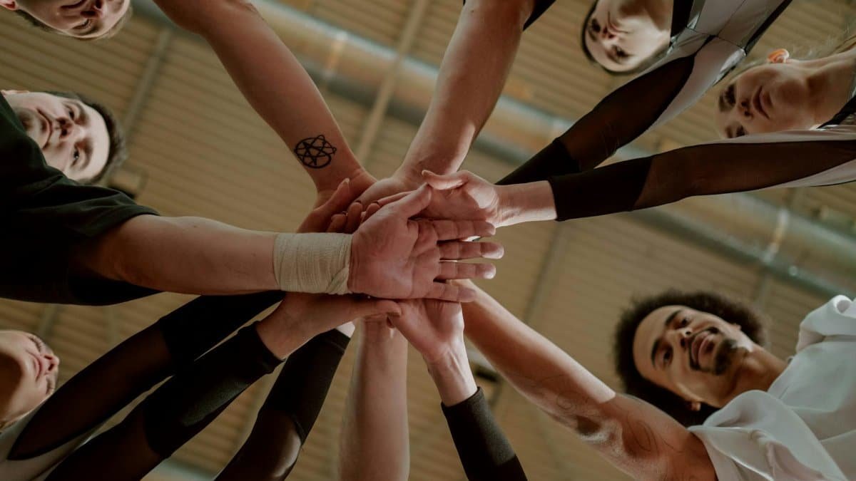 A diverse group of people joins hands in a supportive team gesture from a low angle.