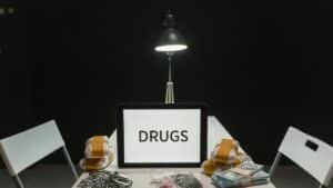 A dimly lit room with a sign displaying 'DRUGS' surrounded by money and illegal substances.